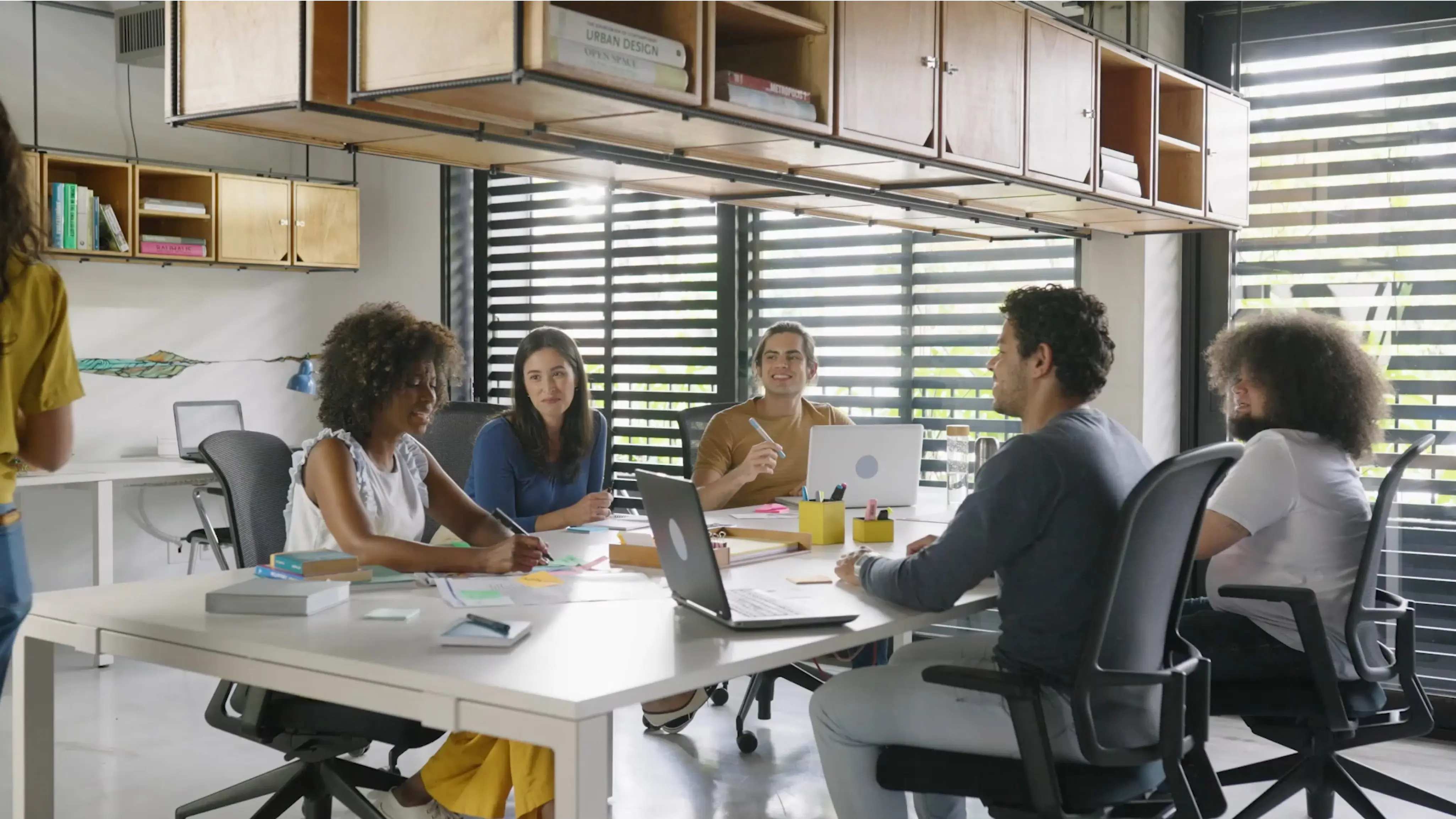 Team meeting around white rectangle table with work equipment